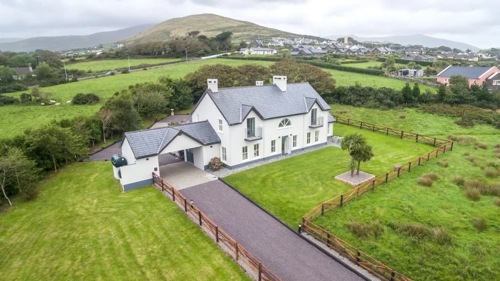 Aerial view of a white house, gate lodge and lawn with a mountain behind